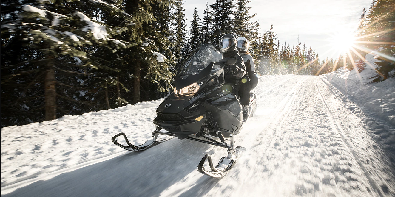 Riders two up on a snowmobile riding down a groomed forest trail
