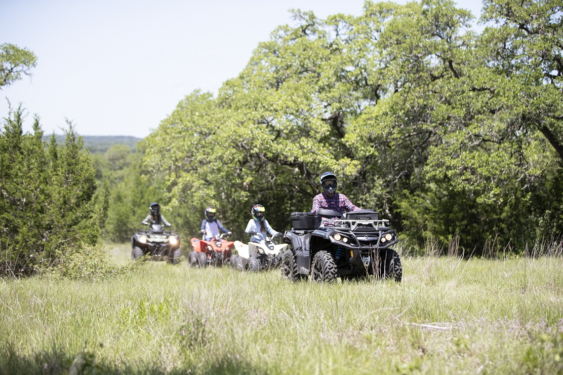 Riders on ATVs travel down a trail in a single file line